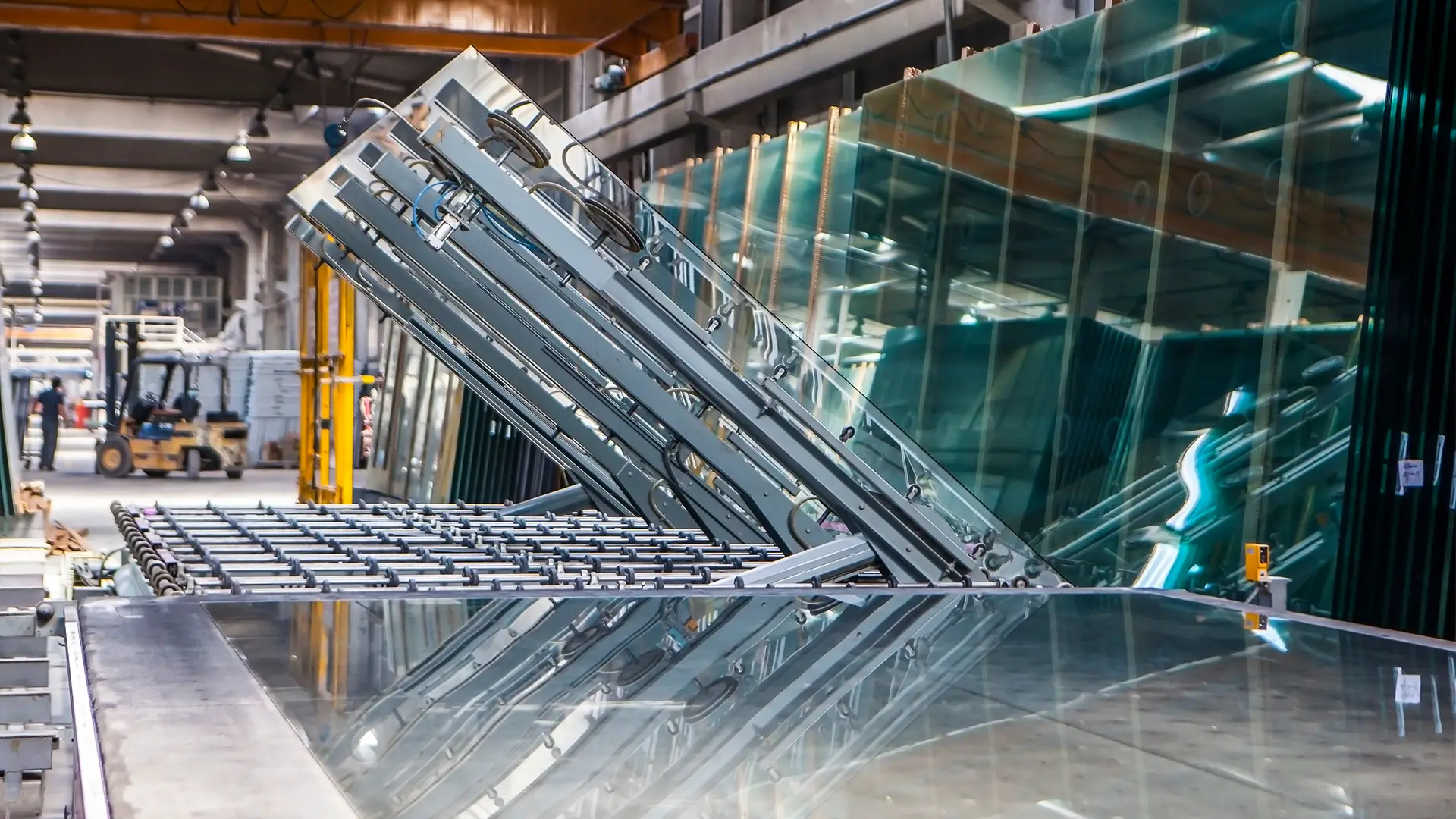 Robotic vacuum suction arms lifting large glass panels in the KJbath factory with glass storage racks and forklift behind