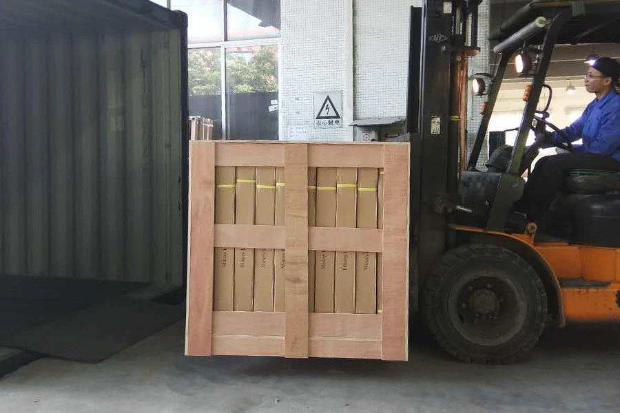 Orange forklift loading a wooden crate of boxed products into a shipping container at the factory