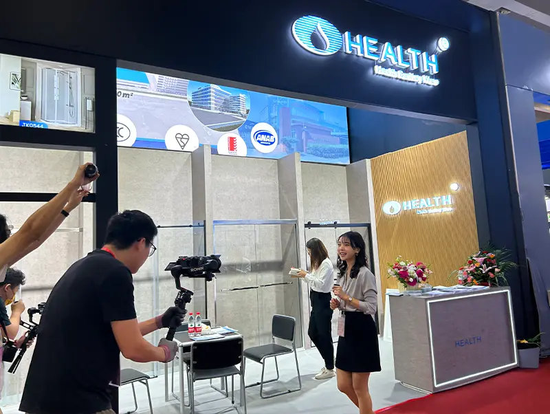 HEALTH branded exhibition booth with glass shower enclosure displays, LED screen and red carpet reception area