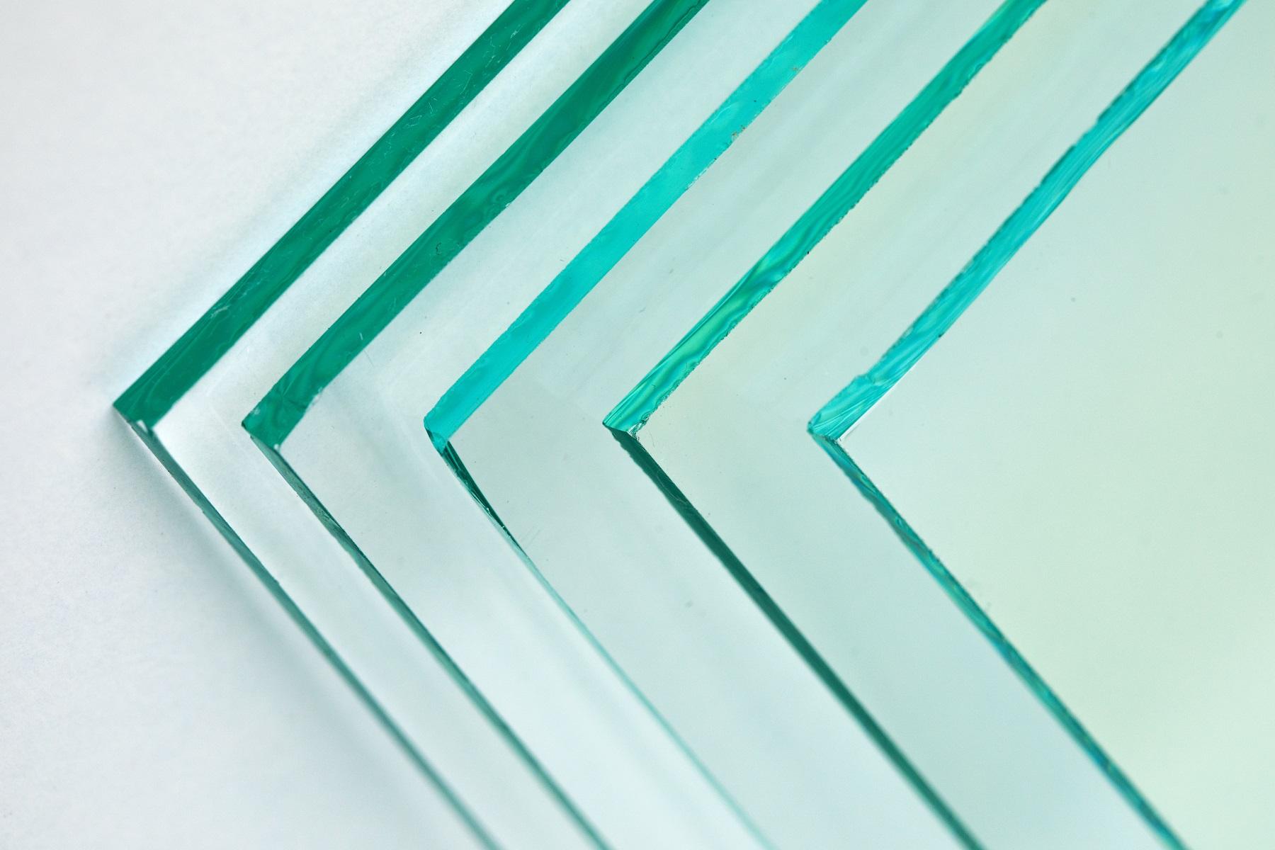 Close-up of four overlapping tempered glass sheets showing green tinted polished edges on a white surface