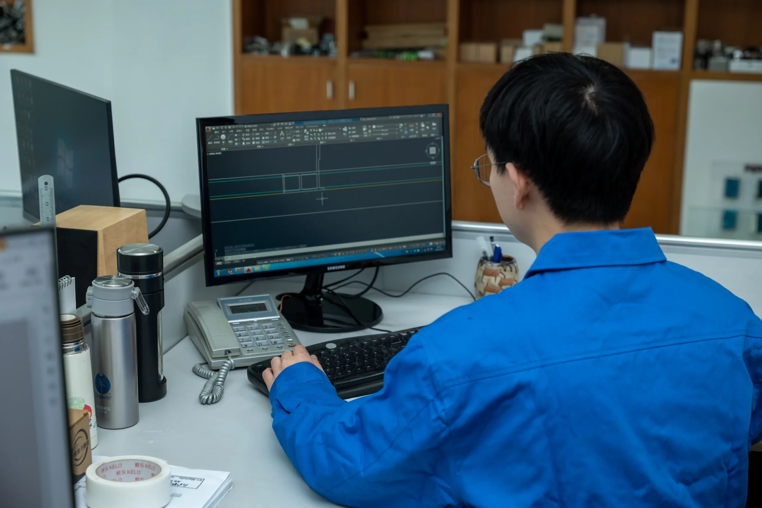 KJbath engineer in a blue uniform working on CAD design software at a technical workstation with a Samsung monitor