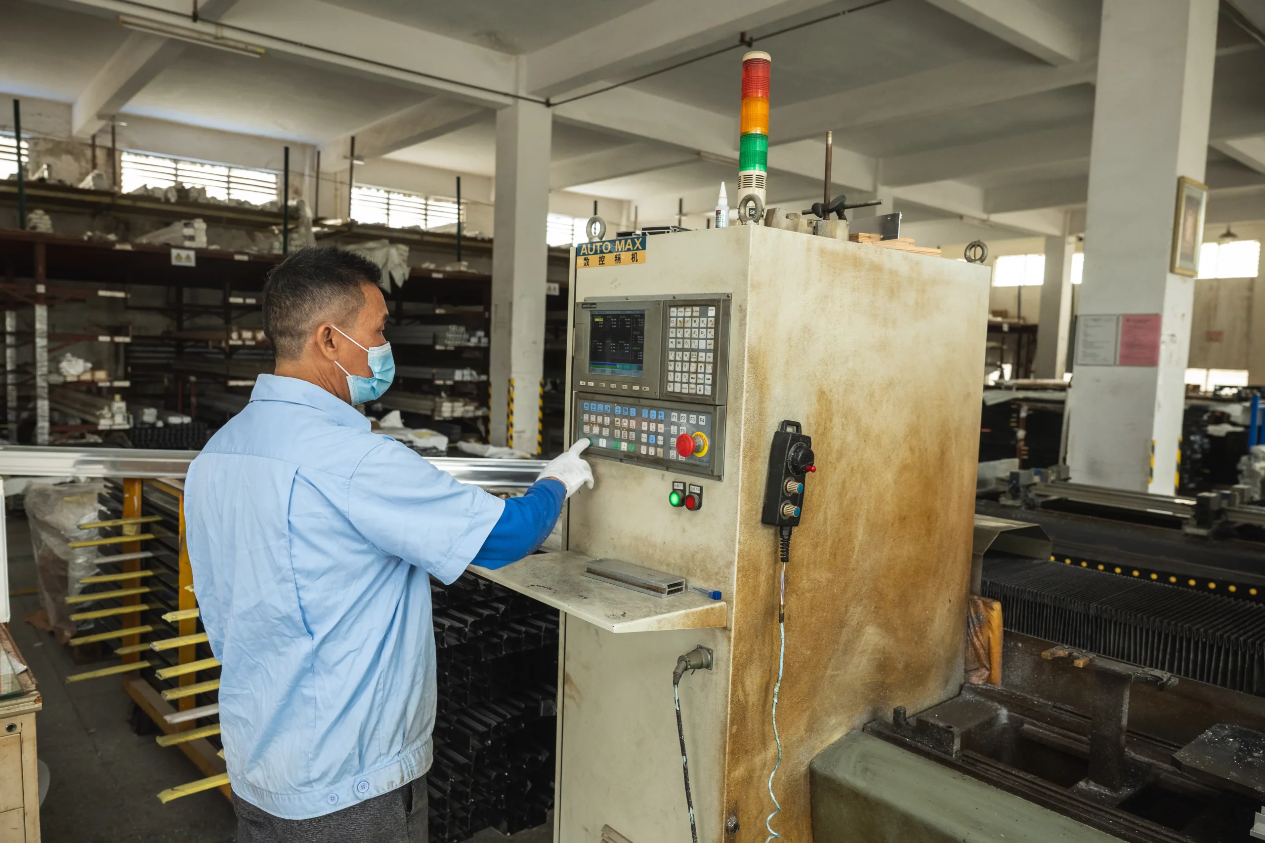 KJbath factory worker in blue uniform pressing buttons on an AUTO-MAX CNC machine control panel