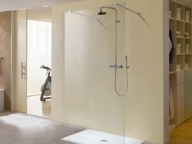 Frameless glass shower enclosure with white tray, chrome rainfall showerhead and handheld wand in a bright modern bathroom