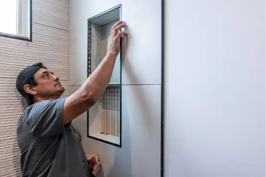 Installer fitting a black-framed recessed shower niche into large white wall tiles for a labor-saving bathroom installation