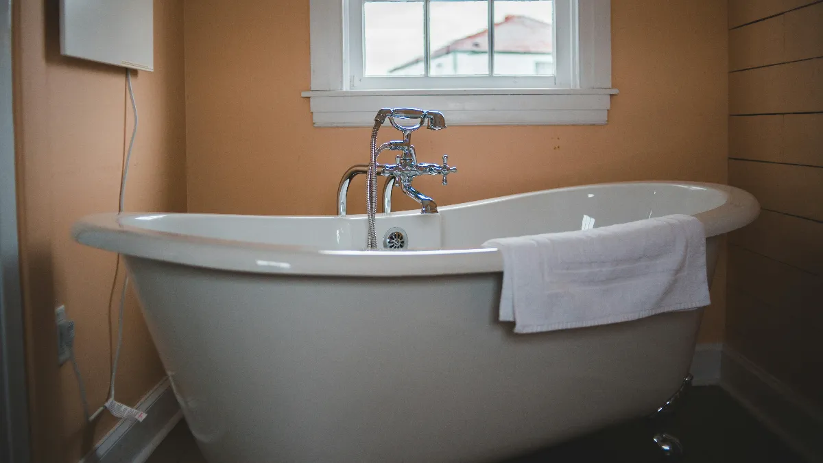 White acrylic clawfoot freestanding bathtub with vintage chrome cross-handle faucet in a warm-toned cozy bathroom