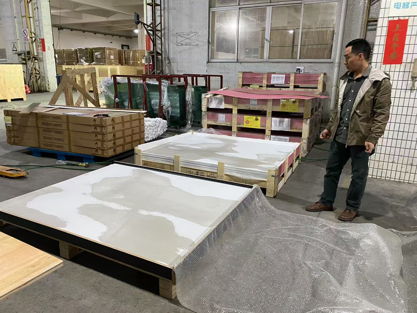 Inspector checking large flat panels wrapped in bubble wrap and stacked on wooden pallets inside a distribution warehouse