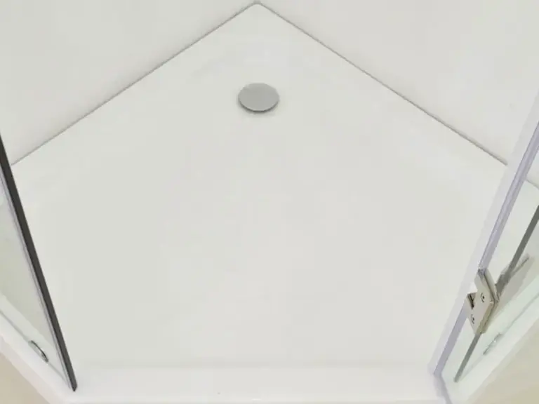 Top-down view of white corner shower base with flush chrome drain and glass panel hinges in a frameless enclosure