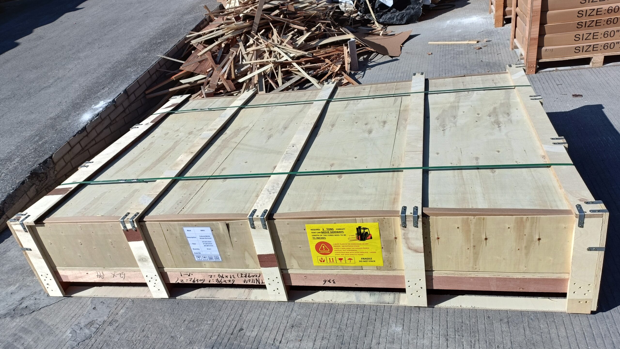 Reinforced wooden export crate with metal corner brackets, green strapping, and FRAGILE DO NOT STACK handling labels on a paved yard