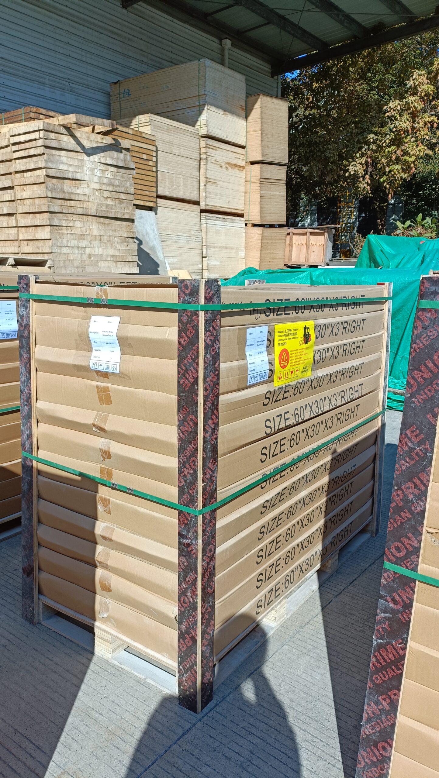 Tall wooden export crate wrapped in green strapping with corner protectors, stacked on a pallet beside more crates