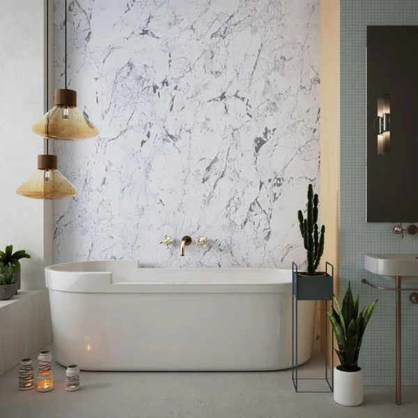 White oval freestanding bathtub with gold wall-mounted faucet against a white marble accent wall in a cozy bathroom