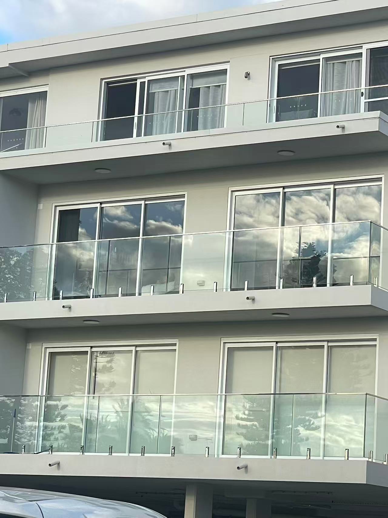 Modern Australian apartment building exterior with glass balcony balustrades and sliding glass doors under daylight